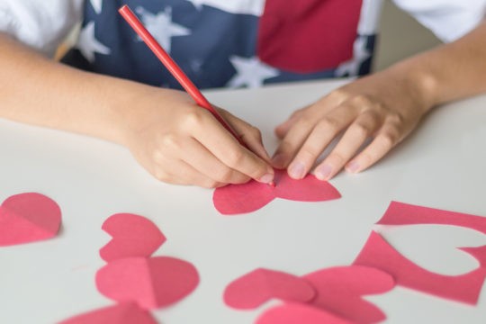 Young boy writing on paper heart cut-outs.