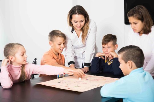Teacher standing over a group of young students at a table playing a review game