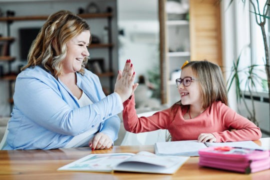 Young girl and mom high-fiving while working on homework.